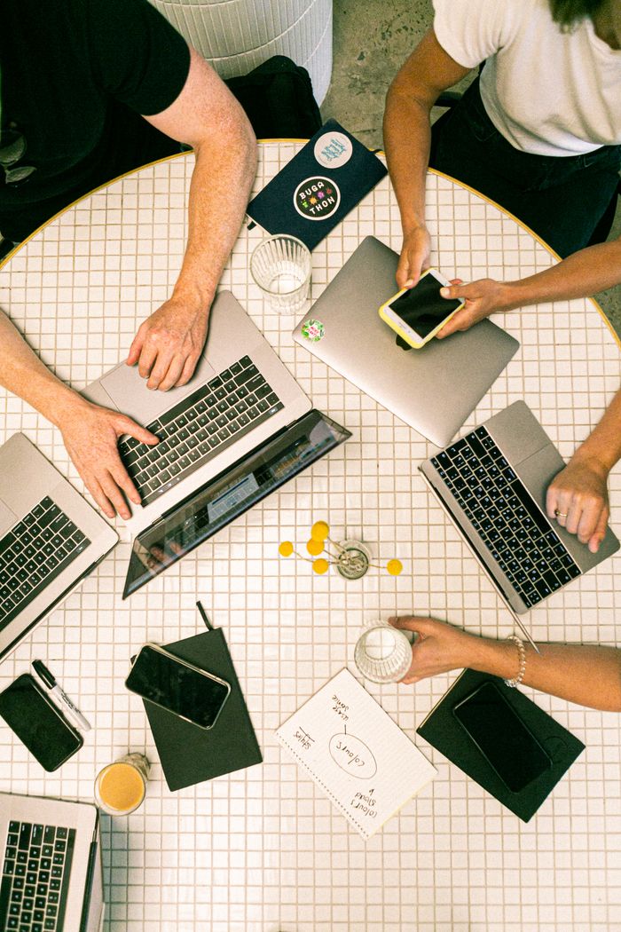 about-us-01 Vue plongeante d’une équipe qui collabore avec des ordinateurs portables, des téléphones et des notes dans un bureau moderne.